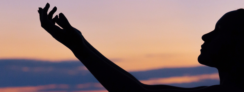 Silhouette of a woman raising her hands against a sunset