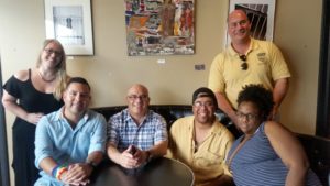 Members of The Arc Mercer's SNAP program supporting LGBTQ individuals, including executive director Steve Cook, are seated on a couch smiling for the camera. 