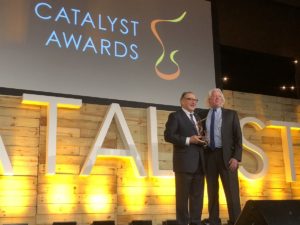 Jack Robinson accepts his Catalyst Award on stage, posing with presenter Fred Misilo.