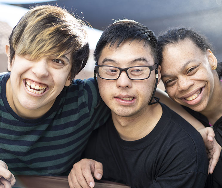 Three young men with intellectual disabilities hugging and smiling at the camera