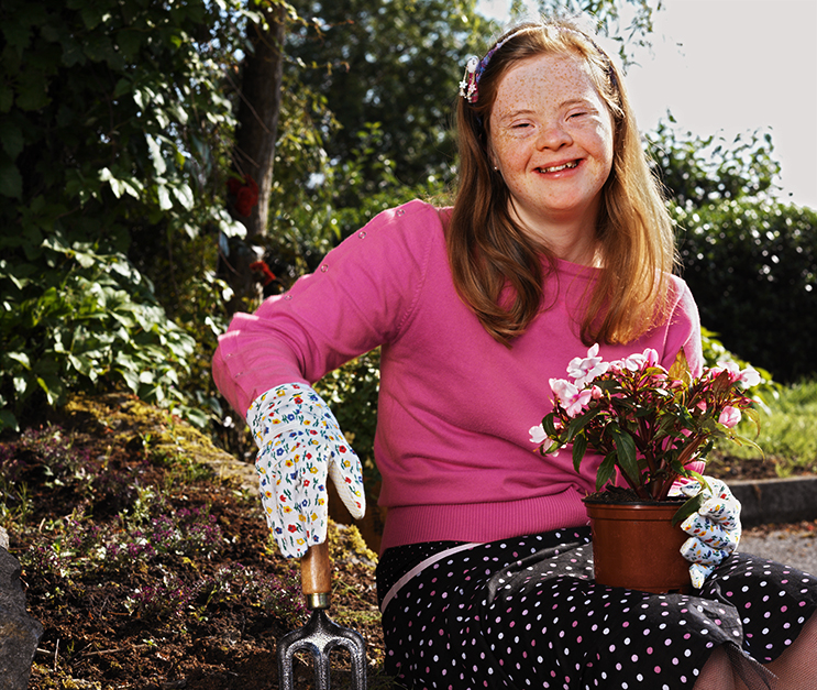 Teenage girl with down syndrome gardening, holding a flower pot and smiling