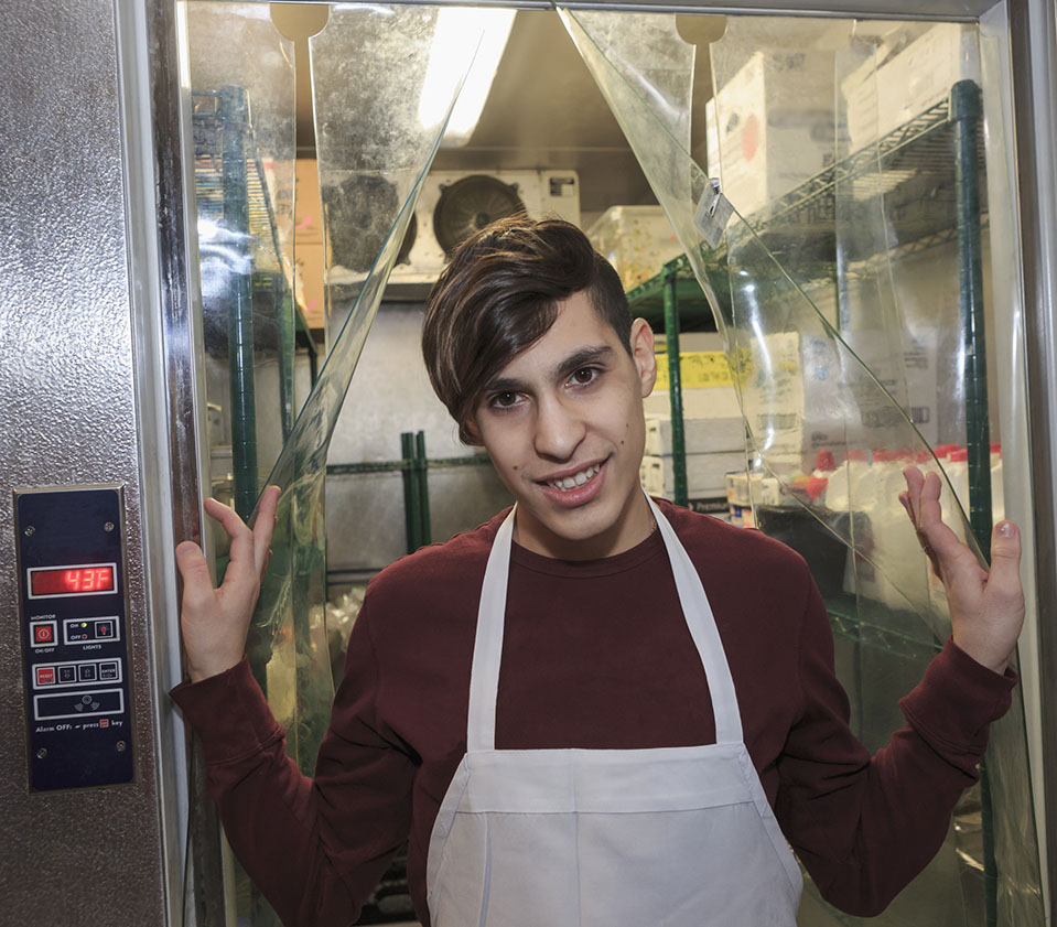 Young teenage boy with a disability wearing apron and standing in restaurant supply closet
