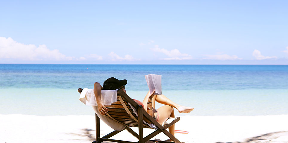 Woman reading a book and lounging in a beach chair in the shade looking toward the ocean