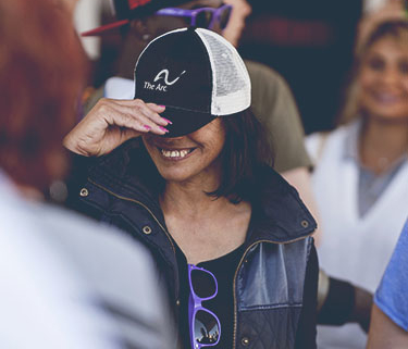 Smiling woman wearing a hat with The Arc's logo pulled down over her eyes