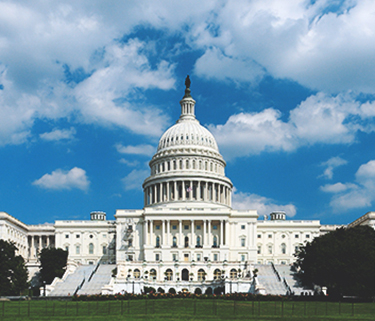 The United States Capitol building with green lawn in forefront and blue, cloudy sky in background
