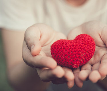 Two outstretched hands holding a knitted, red, stuffed heart