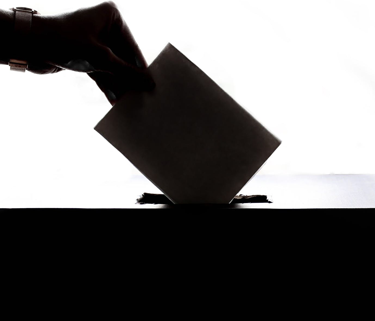 silhouette of a hand casting a paper ballot into a box