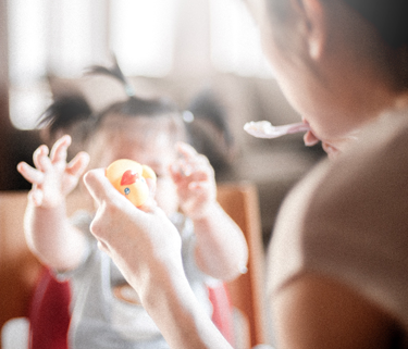 Out of focus image of a woman feeding a baby and holding a rubber ducky