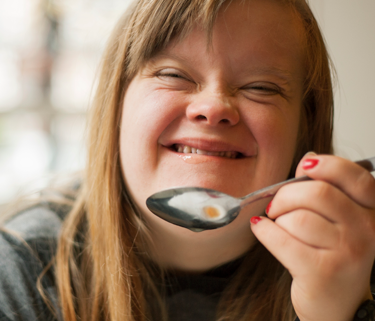A young girl with down down syndrome smiles while holding a spoon