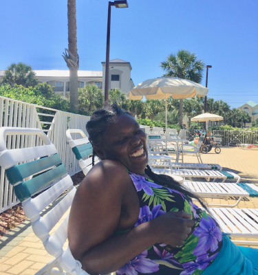 A woman in a floral bathing suit lays in a beach chair by the pool, smiling