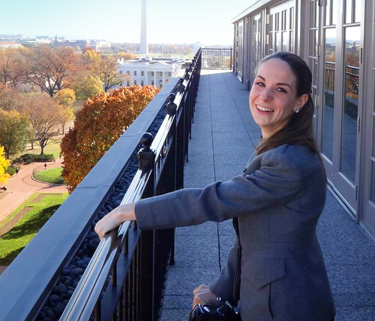 A woman smiles from a rooftop with the Washington Monument in the background