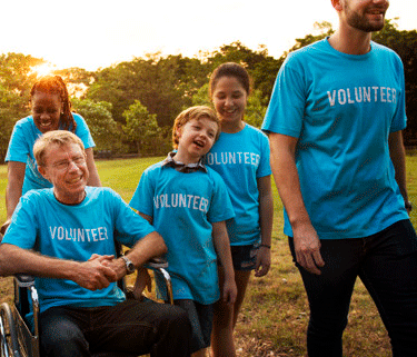 a group of people of varying ages walk on a field with sunset in the background. They all wear blue shirts that say "volunteer".