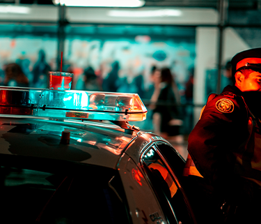 A cop standing in front of his cop car outside at night.