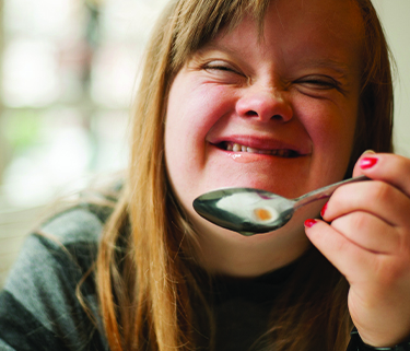 A photo of a woman holding a spoon close to her mouth and laughing