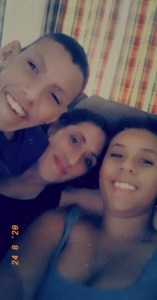A selfie of a mother and her two teenage children on a couch, with checkered blinds in the background. 