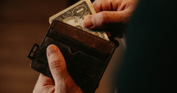 Close up of a person holding a small leather wallet in their left hand and pulling out a folded dollar bill