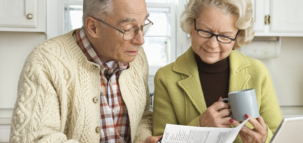 Older couple is seated and looking down at a trust document; the woman is holding a coffee mug