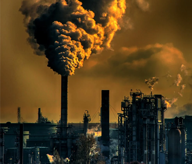A photo of an industrial plant with an orange sky and smoke plumages coming out of smoke stacks on the buildings.