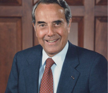 A headshot of a smiling former Senator Bob Dole in front of a wooden wall.