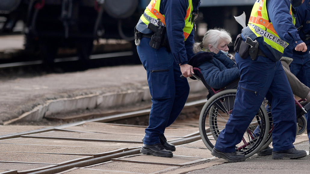 Tw police officers escorting a woman in a wheelchair across train tracks in Ukraine.
