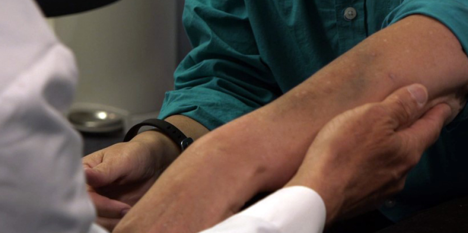 A close up image of a person in a white doctor's jacket. The photo only shows the doctor's hand holding the arm of a patient while they are being examined.