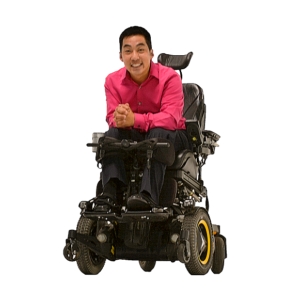 A man wearing a pink button down shirt smiles and is in a motorized wheelchair. 