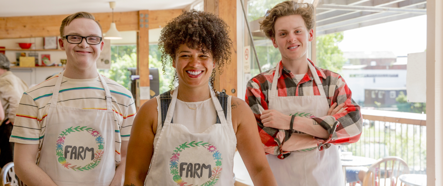 Three young adults wearing aprons smile at the camera.