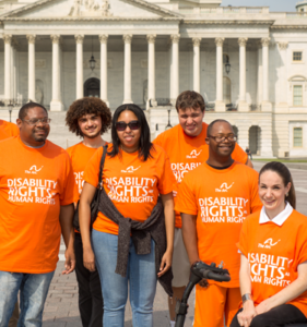 A group of people in front of the Capitol in Washington, DC. They are all wearing orange T-shirts with white letters that say "Disability Rights Are Human Rights."
