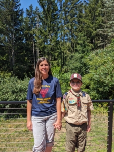A mother and son standing outside in a park. The son is wearing a boy scout uniform.