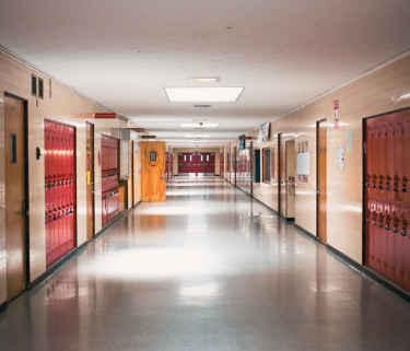 A long school hallway lined with red lockers and classroom doors on either side.