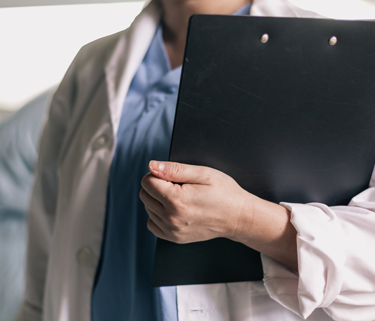 A medical professional in a white labcoat holds a black clipboard.