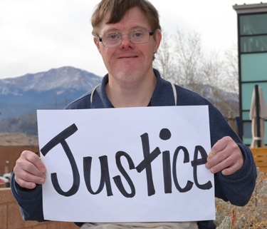 A man with a disability holds a sign up that says "Justice."