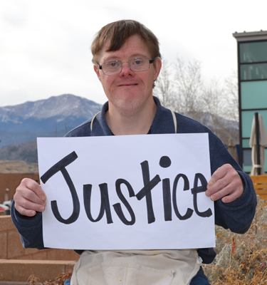 A man with a disability holds a sign up that says "Justice."