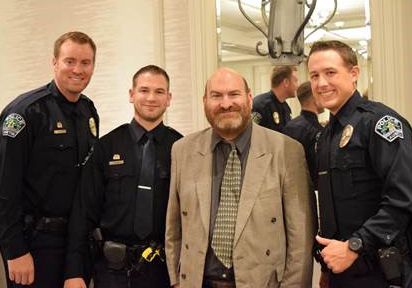 James Meadours, a man with a disability, is standing next two three police officers at an event. They are all smiling.