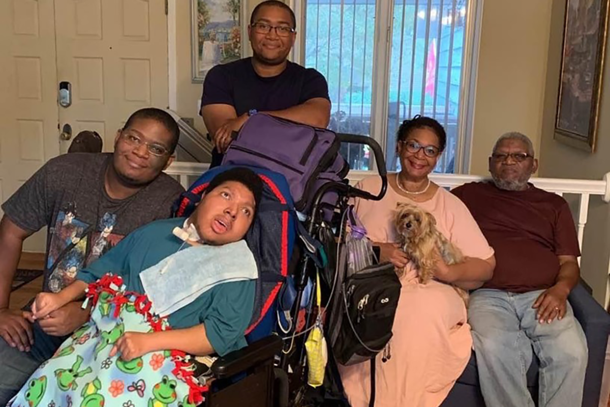 A family, parents and three sons, posing for a photo in a living room. One of the sons has disabilities and is in a wheelchair.