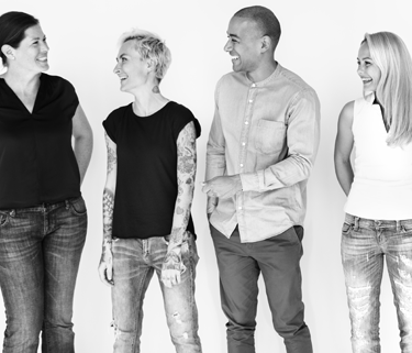 The image is in black and white. There are four adults standing against a white background. They're smiling and looking at each other.