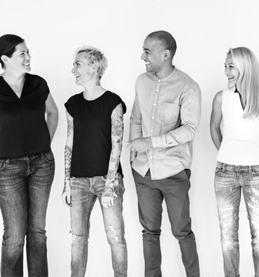 The image is in black and white. There are four adults standing against a white background. They're smiling and looking at each other.