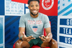 Lawrence Sapp sitting on a bench, wearing a "Team USA" t-shirt and smiling.
